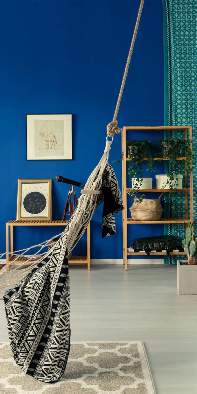 Colourful bohemian interior with a hammock chair, patterned textiles, plants and collected decor