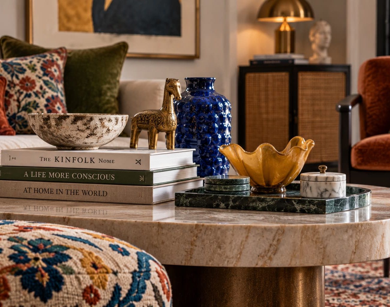 Eclectic interior detail featuring colourful ceramic vessels, sculptural brass objects, books, marble, patterned textiles and contrasting materials