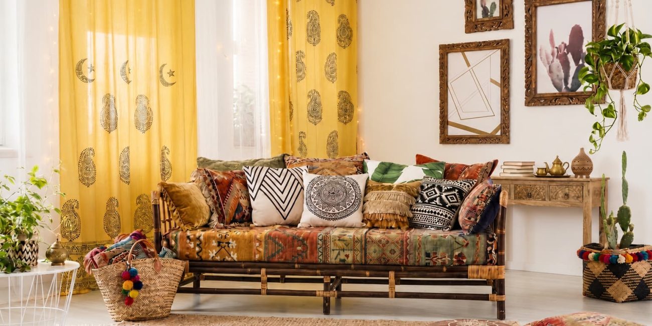 Colourful Bohemian living room with a patterned sofa, eclectic cushions, yellow paisley curtains, plants and handcrafted décor.